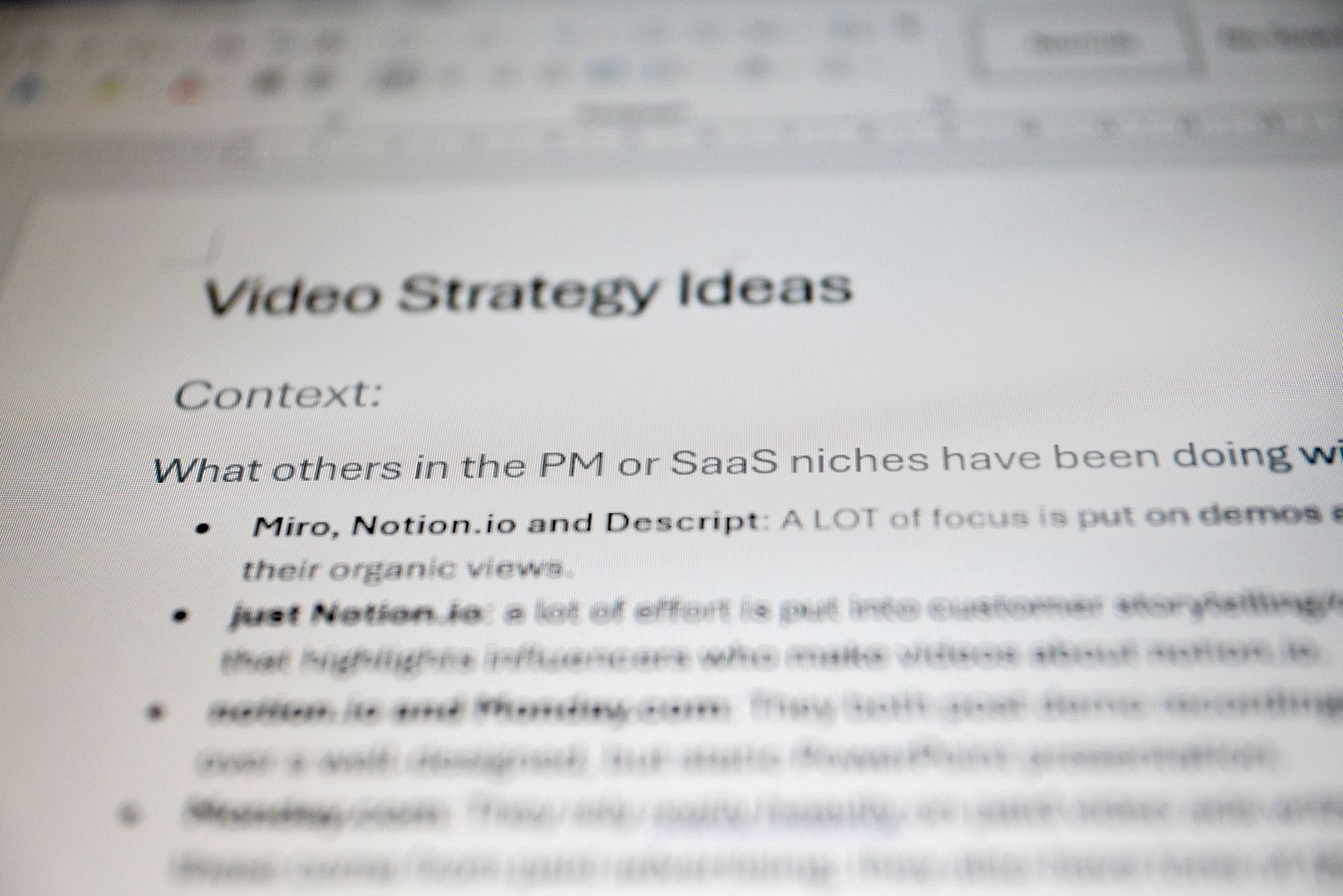 Blurred close-up of the 'Video Strategy Ideas' competitor research document, referencing Miro, Notion.io and Descript